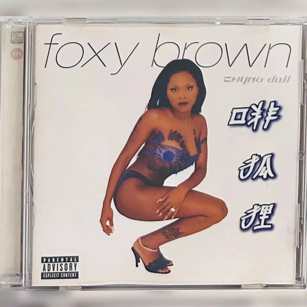 CD cover featuring Foxy Brown. She is crouching with her right arm extended and her left arm bent at the elbow. She is wearing a blue bathing suit and black heels. The background is white with her name written in script font. "Chyna Doll" is also written in script next to her name. To the right of Foxy Brown are three lines of Chinese characters. At the bottom left of the cover is the parental advisory logo.