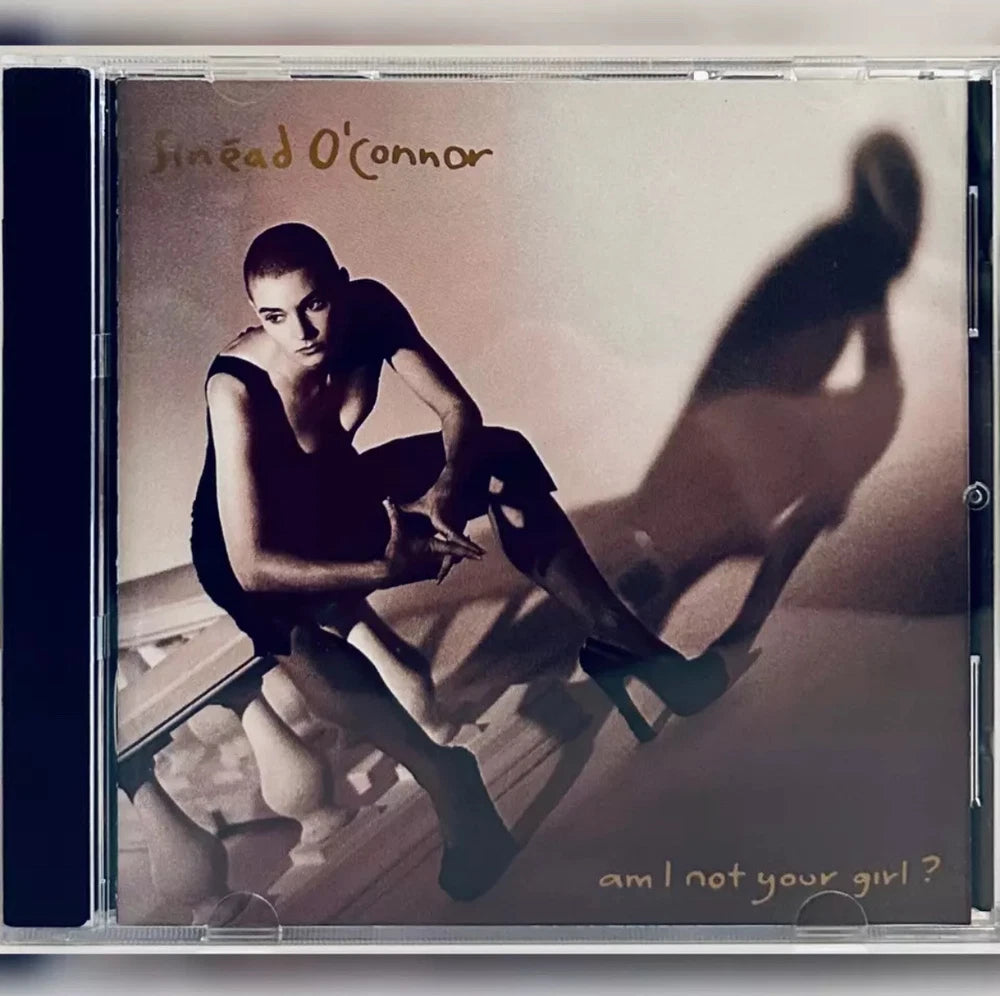 CD cover featuring Sinéad O'Connor in a black dress, high heels, and a shadow figure with the album title "am I not your girl?".
